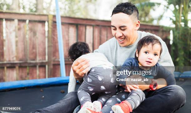 father with twin kids on trampoline. - maori greeting stock pictures, royalty-free photos & images