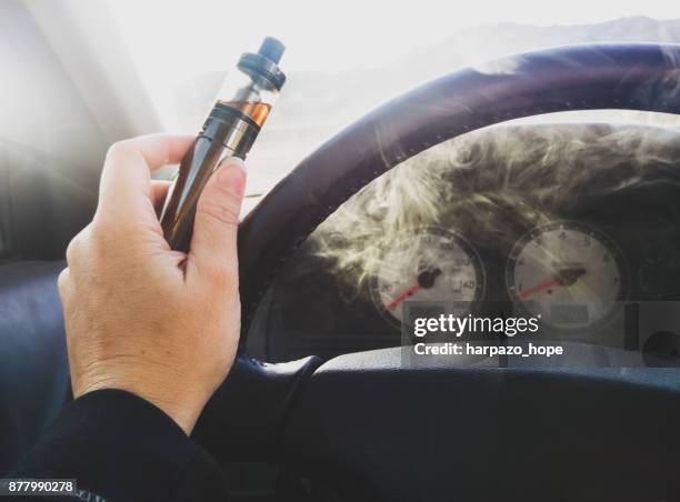 woman's hand holding electronic cigarette in a car. - vaping stock pictures, royalty-free photos & images
