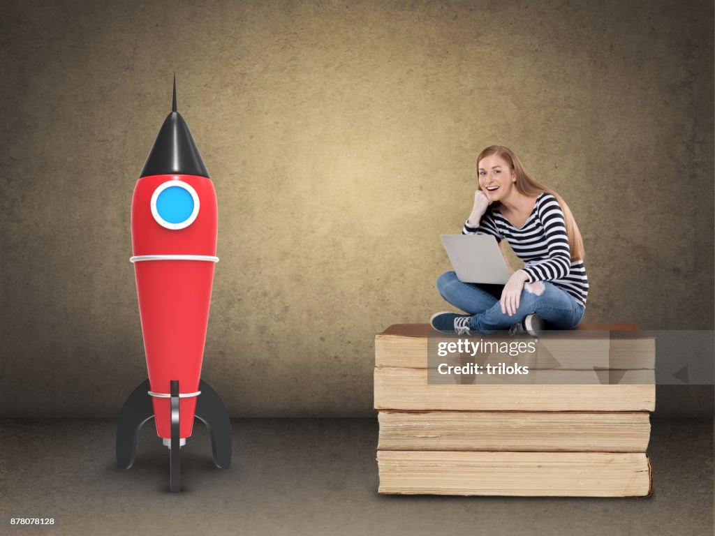 Excited female student with laptop on stack of books