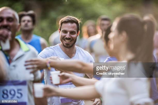 Happy man taking fresh water from volunteers during marathon race in nature.