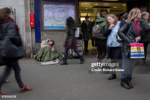 As passers-by blur when walking past, a homeless street beggar sleeps on the ground outside Holborn tube station, on 22nd November 2017, in London...