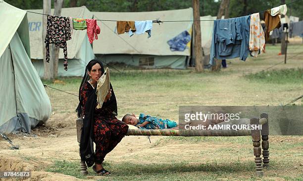 Pakistani internally displaced woman, fleeing from military operations against Taliban militants in troubled Swat valley and Buner, fans her children...
