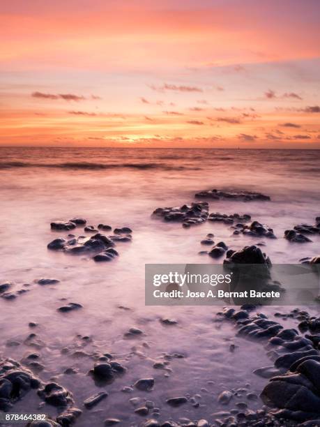 exit of the sun with a sky of clouds of orange color, on the surface of the sea, in a zone of coast with rocks and waves in movement. tabarca island,  mediterranean sea, spain - tabarca stock pictures, royalty-free photos & images