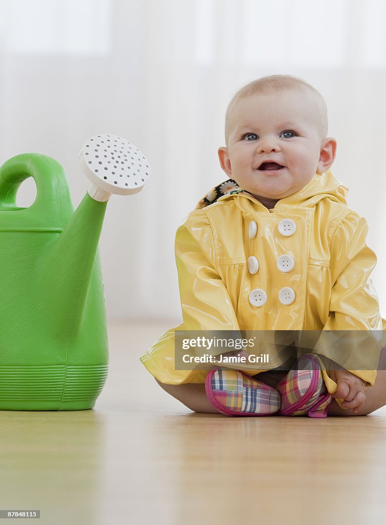 Baby girl in raincoat next to watering can