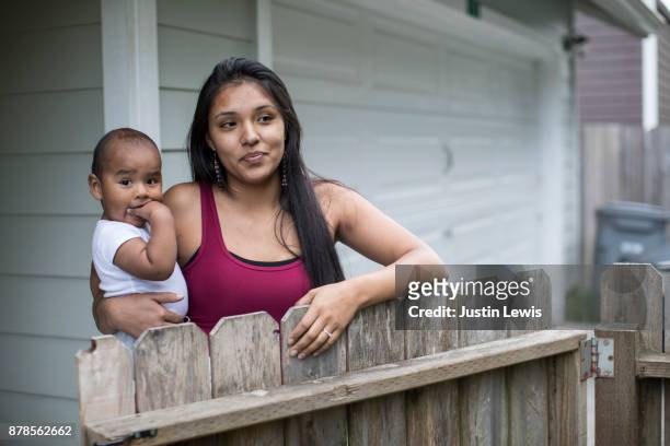 young, modern, native american mom holds baby at front gate to their home - baby gate stock pictures, royalty-free photos & images