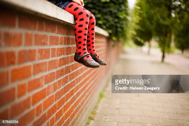child sitting on red brick wall in dotted tights - skimpy girls stock pictures, royalty-free photos & images