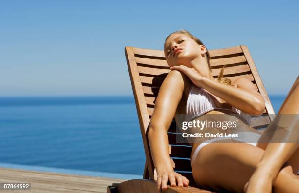 young woman in bikini lying on sun lounger by sea - tomar el sol fotografías e imágenes de stock