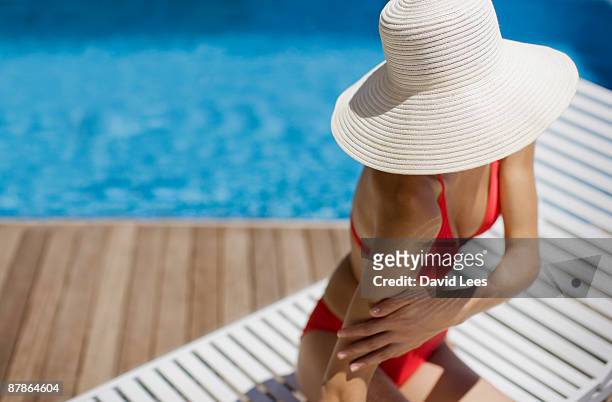 young woman applying  sunscreen by swimming pool - cappello per il sole foto e immagini stock