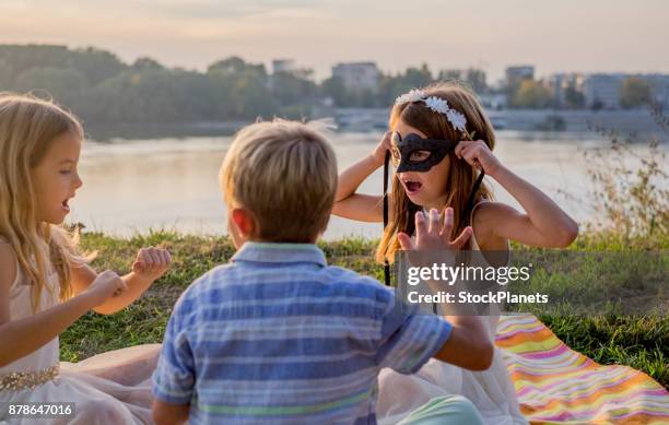 children sitting and playing with mask at riverbank - triplet girls stock pictures, royalty-free photos & images