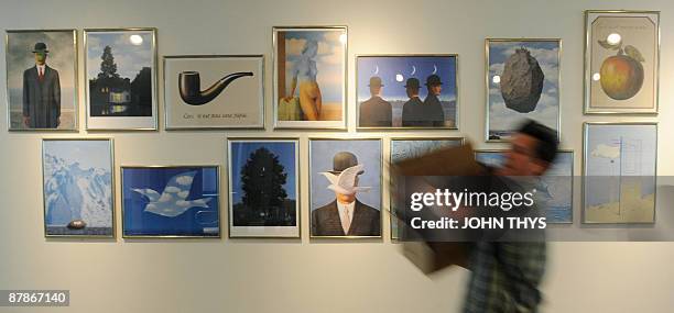 Man carries a box past prints of paintings by the Belgian artiste Rene Magritte at the press opening of the new Margitte museum in Brussels on May...