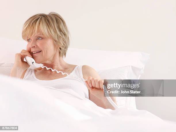 mature woamn in bed on telephone - landline phone woman stock pictures, royalty-free photos & images