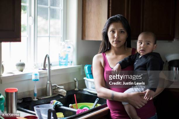 young, modern native american mom and baby washing dishes in their kitchen - family serious stock pictures, royalty-free photos & images