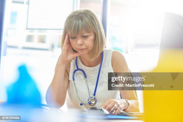 stressed female doctor sat at her desk - general practitioner stock pictures, royalty-free photos & images