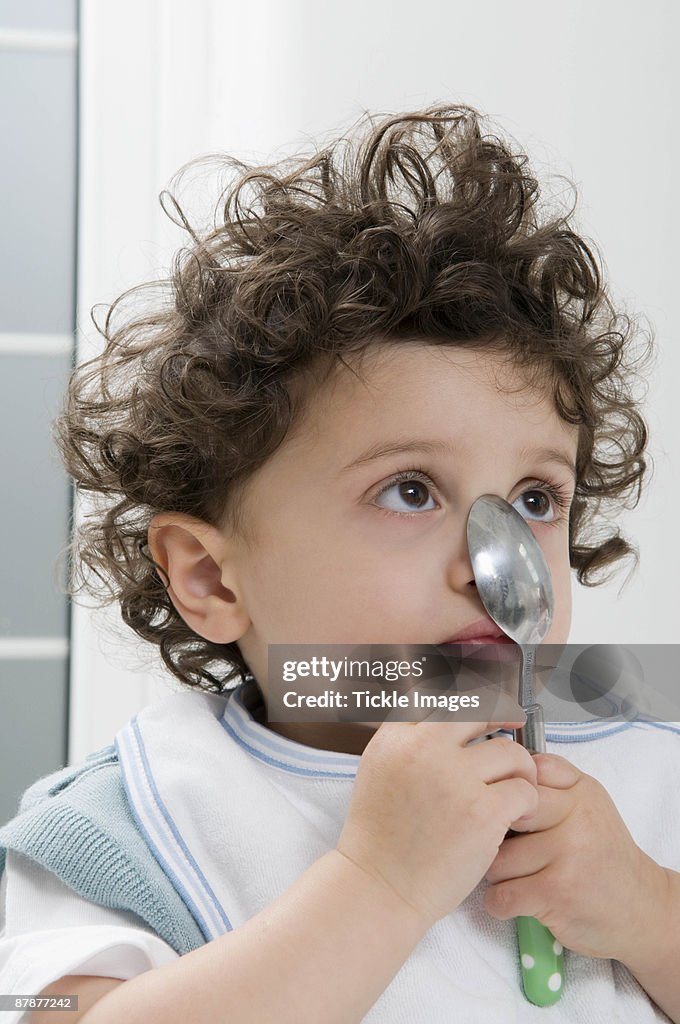 A boy holding a spoon on his nose.