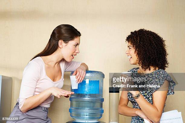 two women are chatting by water cooler - trinkwasserbehälter stock-fotos und bilder