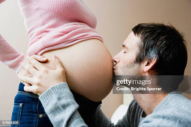 man kissing woman's pregnant stomach - mittlerer teil stock-fotos und bilder