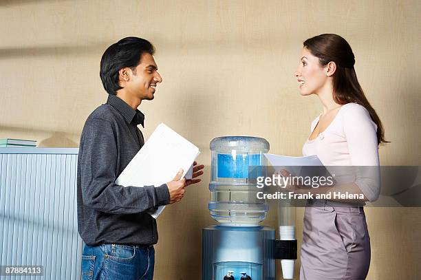 man and woman chatting by water cooler - dispensador de agua fotografías e imágenes de stock