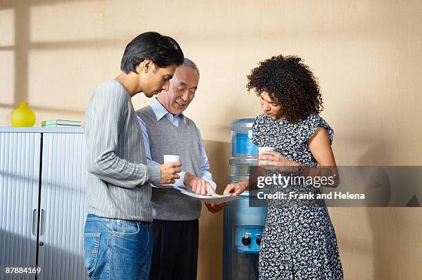 office workers standing by water cooler - dispensador de agua fotografías e imágenes de stock
