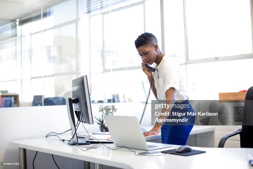 Businesswoman using phone and laptop in office