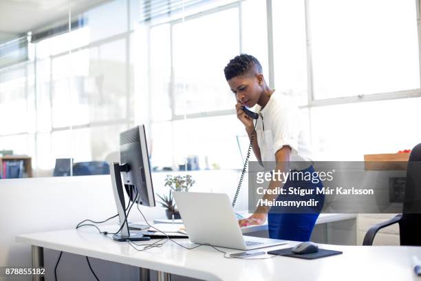 businesswoman using phone and laptop in office - landline phone imagens e fotografias de stock