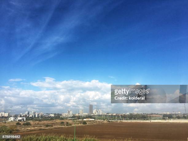 harvested fields under blue sky with distant view of city skyline - sichelspötter stock-fotos und bilder