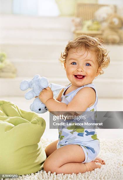 laughing baby kneeling and shaking a teddy bear - bébé doudou photos et images de collection