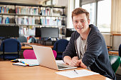 Portrait Of Male Student Working At Laptop In College Library