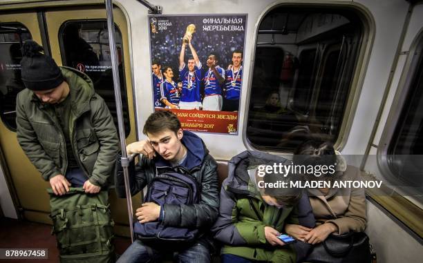 Commuters sit under a FIFA World Cup 2018 Finals Draw Ceremony announcement poster depicting the French National football team winning the Trophy...