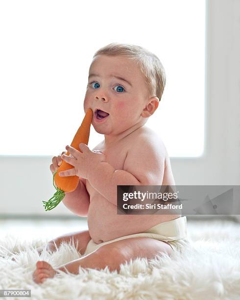 baby boy holding toy carrot - baby eating toy foto e immagini stock