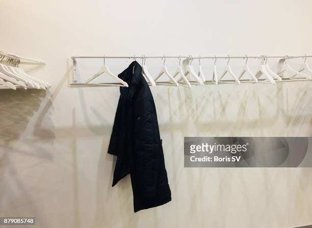 white empty hangers with one black coat - placard fotografías e imágenes de stock