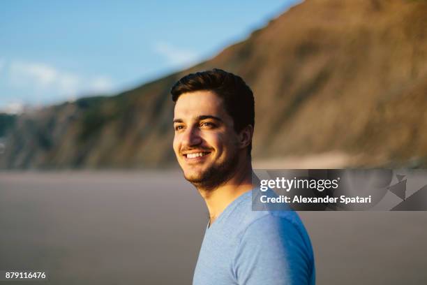 portrait of a young smiling happy man - hispanic man on beach stock-fotos und bilder