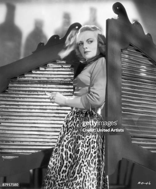 American actress Jeanne Cagney standing by the doors of a saloon, wearing a leopard-print skirt and holding a cigarette, in a promotional portrait...