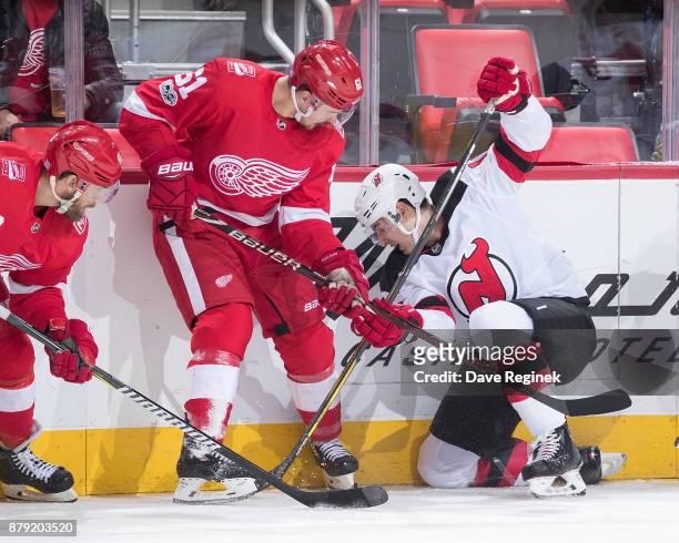 Steven Santini of the New Jersey Devils battles for the puck along the boards with Xavier Ouellet of the Detroit Red Wings during an NHL game at...
