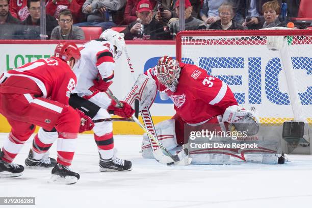 Goaltender Petr Mrazek of the Detroit Red Wings makes a stick save on Miles Wood of the New Jersey Devils as Xavier Ouellet of the Red Wings defends...