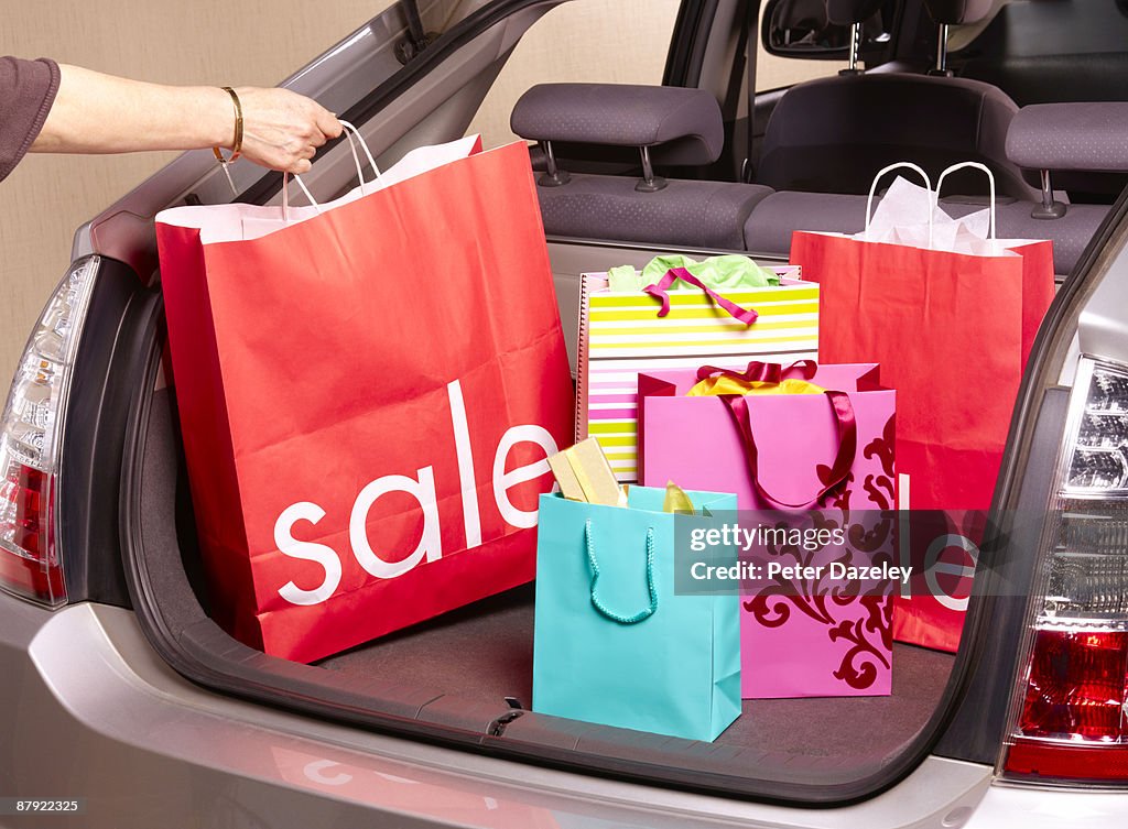 Woman putting sale carrier bag in car boot.