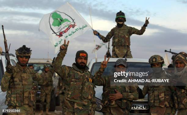 Iraqi paramilitaries of Asa'ib Ahl al-Haq, one of the units of the Hashed al-Shaabi , wave their group's flag and flash the victory gesture as they...