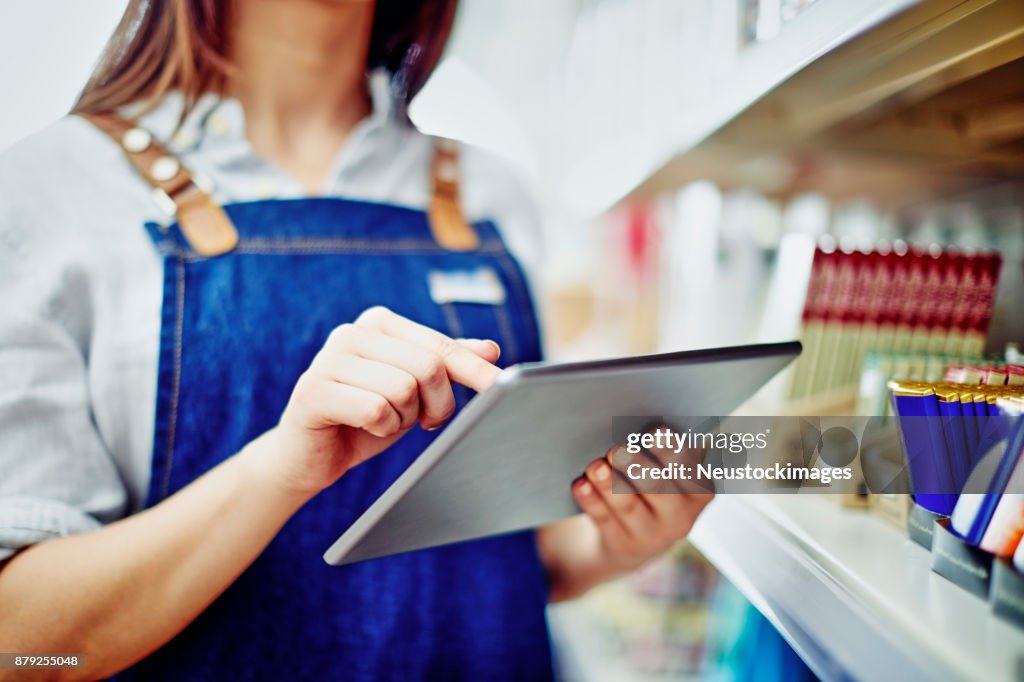 Midsection of deli owner using digital tablet by shelves