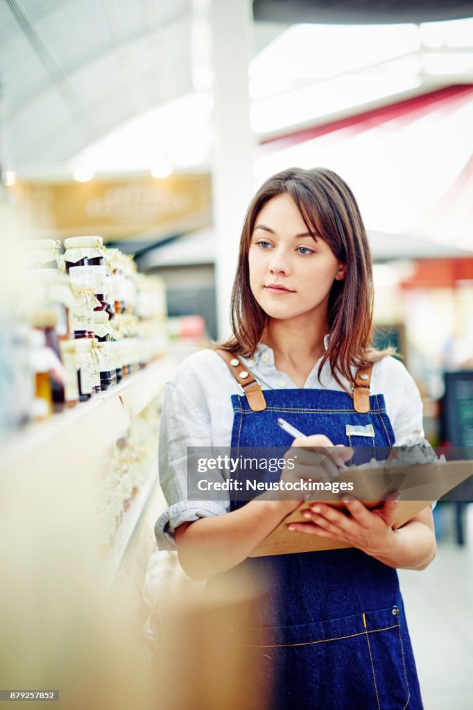 Beautiful deli owner holding clipboard and pen by shelves