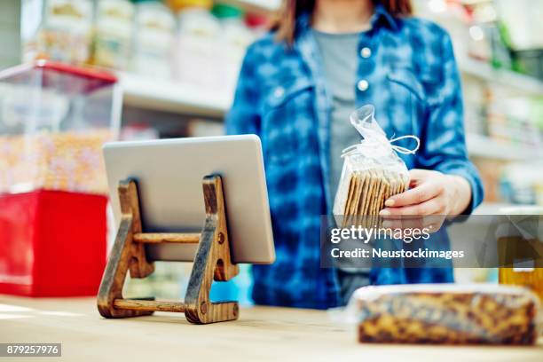 weibliche deli inhaber halten cracker paket von digital-tablette - neustockimages stock-fotos und bilder