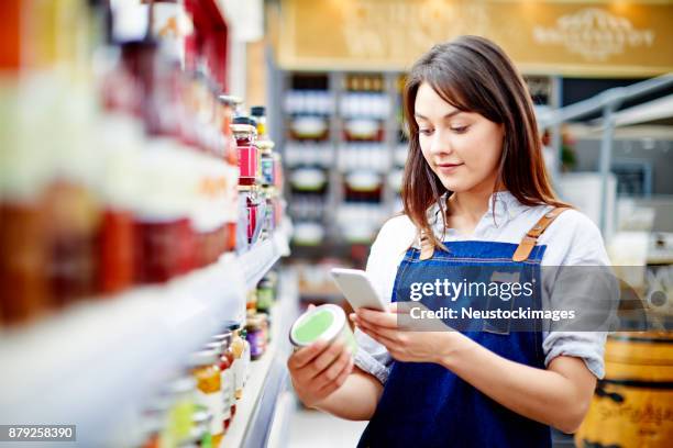 junge verkäuferin etikett auf lebensmittel-container mit smartphone scannen - neustockimages stock-fotos und bilder