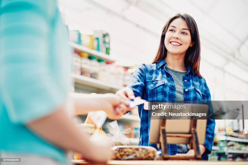 Sonriendo deli propietario recibe tarjeta de crédito del cliente en la tienda