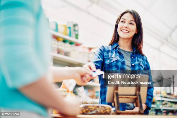 smiling deli owner receiving credit card from customer in store - debit cards credit cards accepted stock pictures, royalty-free photos & images