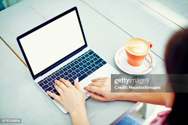 frau mit laptop durch die kaffeetasse am tisch im café - neustockimages stock-fotos und bilder