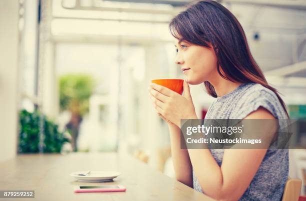 nachdenkliche frau mit kaffeetasse beim sitzen im café - neustockimages stock-fotos und bilder