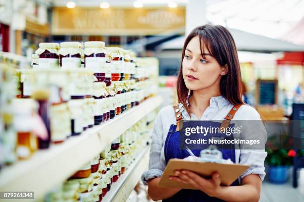 weibliche deli inhaber essen flaschen in den regalen im store prüfen - neustockimages stock-fotos und bilder