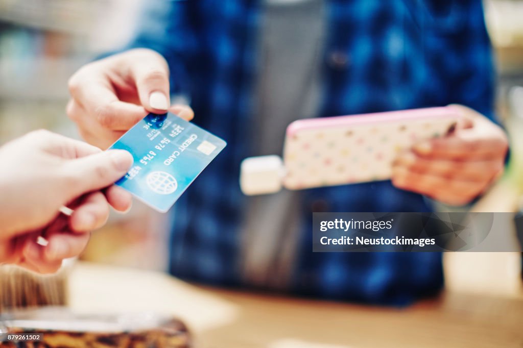 Saleswoman receiving credit card from customer while holding smart phone