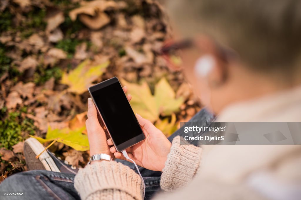 La giovane donna che usa il suo smartphone sullo sfondo delle foglie autunnali.