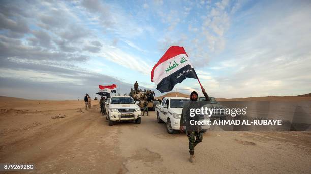 An Iraqi fighter waves the national flag as he walks ahead of pick-up trucks carrying members of the Iraqi forces and supported by members of the...