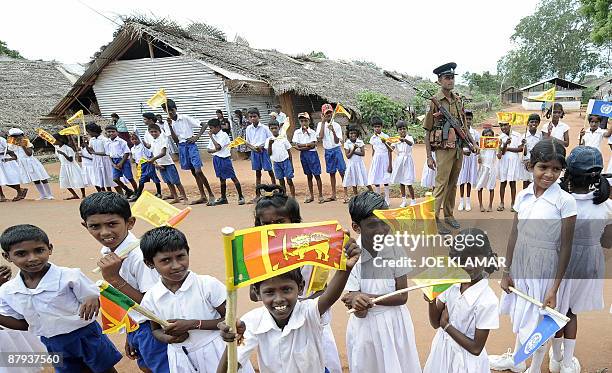 Sri Lankan security official stands guard among uniform-clad internally displaced Sri Lankan children as they wait for a visit by United Nations...