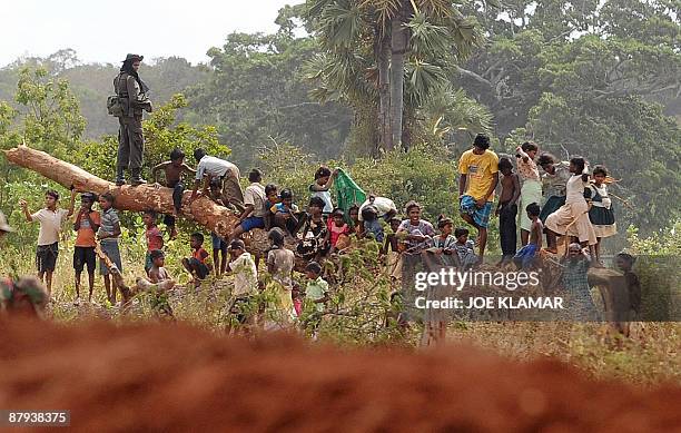 Sri Lankan soldier stands guard as internally displaced Sri Lankan children and people gather on a fallen tree during United Nations...